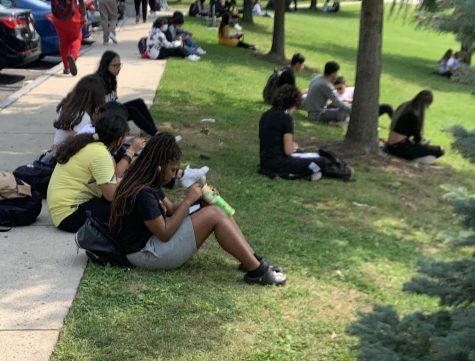 Students enjoy the fresh air, mask break, and each others company as they eat lunch on the grass under the trees.